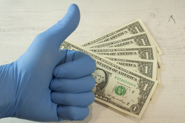 Ludzka ręka w niebieskiej rękawicy ochronnej trzymającej pakiet banknotów i maskę ochronną. - obrazy, fototapety, plakaty