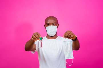 young black man wearing a nose mask and holding out a nose mask and a hand sanitizer