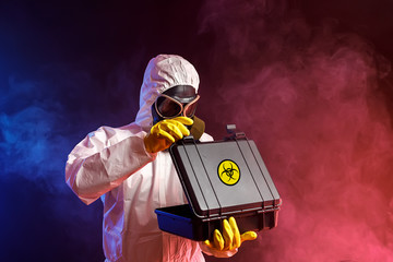 A man in a biological protection suit in a gas mask with a suitcase. Coronavirus