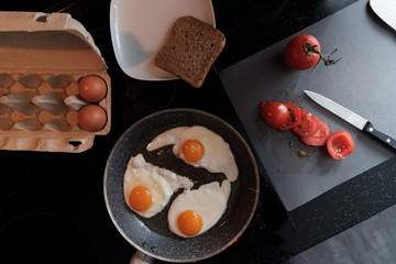 Fried eggs in a frying pan with tomatoes and bread for breakfast on a black background.