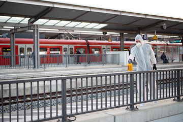 Ein Mann in einem Schutzanzug desinfiziert an einem Bahnhof ein Geländer, Kampf gegen die...