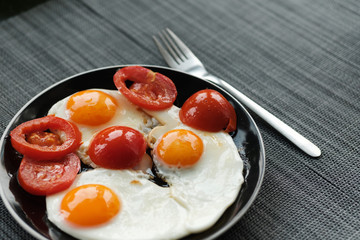 plate of fried eggs with tomato on dark background, top view