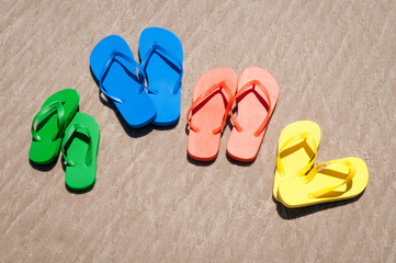 Fototapeta na wymiar Group of flip-flops in bright summer colors sitting on smooth sand beach
