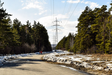 Winding winter forest road. Sunny day in the park. People are walking. Metal poles for high voltage power along the road