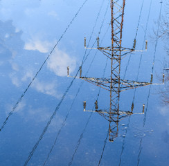 Metal power pole is reflected in water. Image is upside down. Blurry reflection. High voltage...