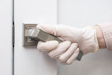 A hand in sterile rubber medical gloves opens the door of a home or hospital. Medical gloves as a means of protection against the virus and covid-19 during the epidemic. The concept of protection