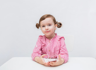 On white background with copy space. A little girl with ponytails in a checked shirt on a white background. The girl listens to music through headphones. The girl listens to music on the phone. 