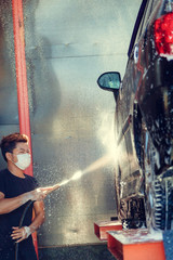 Manual car washing cleaning with foam and pressured water at service station.