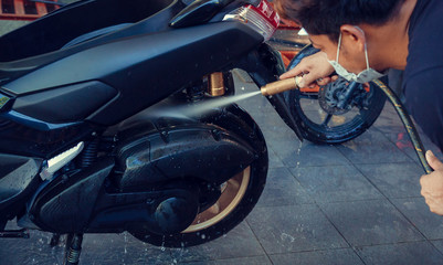 Asian man washing motorcycle or scooter with soap and water at service station or home