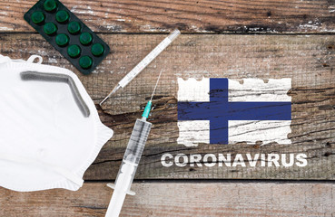 Coronavirus in Finland. Flag of Finland, vaccine, face mask for virus, thermometer, and medicals on wooden table with word coronavirus