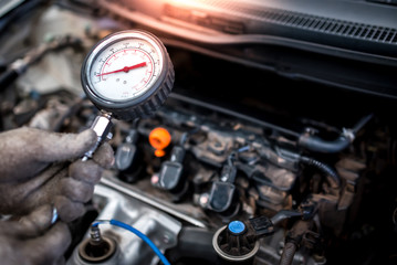 The auto mechanic is about to measure compression in the cylinder of a car engine using a...