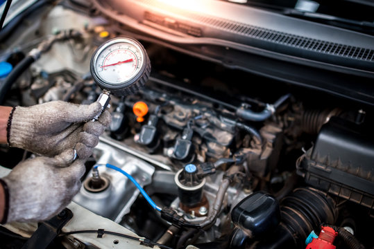 The auto mechanic is about to measure compression in the cylinder of a car engine using a diagnostic barometer and repaired in the engine room for a vehicle.