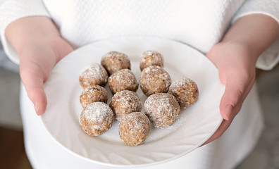 step by step visual instruction how to make energy balls. step 5, Woman holding a plate with ready energy balls. dates and nuts snack for healthy life