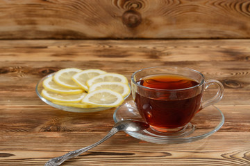 Glasses cup of tea on a wooden table, next to a saucer with slices of lemon.