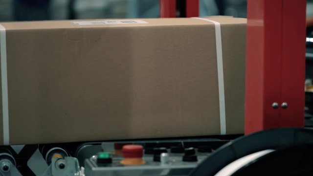 Parcels in a warehouse move along and wait in line the packaging line. Plastic straps are attached with a strapping machine on the package. Automation of online shipping logistics