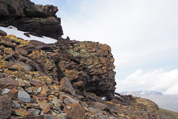 The mountain landscape with the light rocks and stones covered by white snow on the cloudy day.