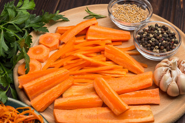 Raw chopped carrots on cutting board. Spices, garlic and parsley on table. Fermented carrots in plate.