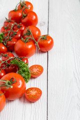 Delicious sweet cherry tomatoes on a stem on white wooden surface with copy space