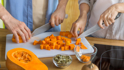 Unrecognizable young couple cutting pumpkin together on kitchen table