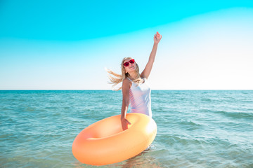 Girl with inflatable rubber enters the sea. Model goes into clear blue water on a hot day and holding orange ring.