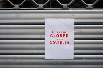 Closeup of information sign on the metallic shutter of the store front : Sorry we are Closed due to covid-19