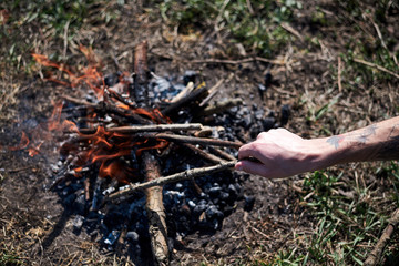 Ternopil/Ukraine-Apr 04 2020: Close-up picture of bonfire, made of dry branches, outside on green grass at sunny weather in summer. Hand, holding wooden stick. fixing fireplace in forest.