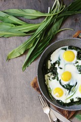 fried eggs with wild garlic as a shakshuka. fried eggs in a frying pan under gray marble on a table, top view. Keto diet dish