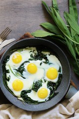 fried eggs with wild garlic as a shakshuka. fried eggs in a frying pan under gray marble on a table, top view. Keto diet dish