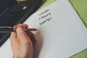 close up of a hand holding a pen with work from home written on a paper in the background