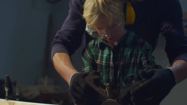 Father teaches his son to use a planer. Paternity