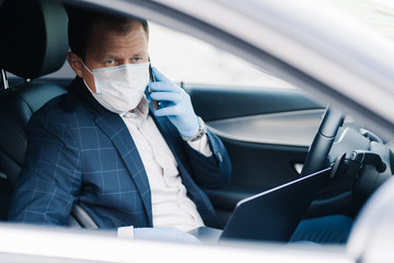 Successful businessman waits for someone in car, puts on medical mask during epidemic as protection...