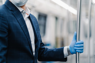Man passenger wears protective medical glove from coronavirus, touches handrail in subway carriage, poses in public transport, dressed formally. Virus, influenza, quarantine and health care concept