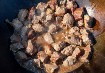 The meat is fried in oil on a cast-iron cauldron.