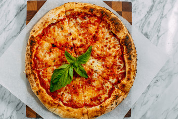 Italian pizza with mozzarella cheese and basil on a marble table
