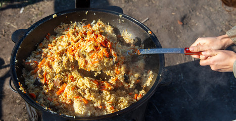 Pilaf with rice is cooked on a cast-iron cauldron.