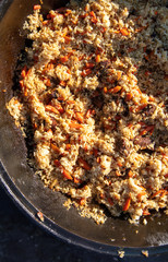 Pilaf with rice is cooked on a cast-iron cauldron.