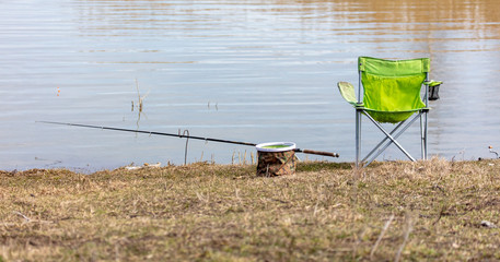 Table, chair and fishing rod on the shore of the pond.