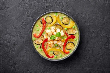 Fototapeta na wymiar Vegetarian Thai Green Curry with tofu in black bowl at dark slate background. Veg Green Thai Curry is thailand cuisine dish with green chillies paste, basil, spices and vegetables. Copy space