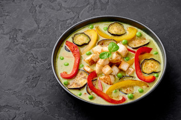 Vegetarian Thai Green Curry with tofu in black bowl at dark slate background. Veg Green Thai Curry is thailand cuisine dish with green chillies paste, basil, spices and vegetables. Thai Food