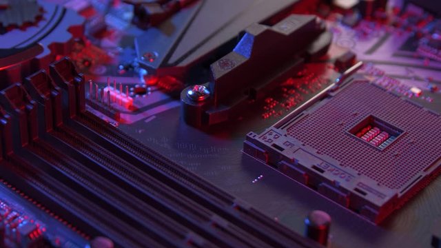 Motherboard with empty processor socket close up pan shot. Computer components on circuit board lit with red and blue ligths.