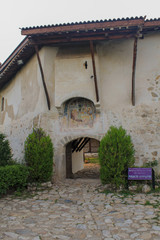 An arch in an old stone wall with an old mural above it and a road lined with large stones