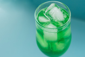 A glass of green cocktail with ice on a blue background.Tableware for alcohol.A glass for champagne and wine.Chilled drinks.
