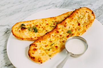 garlic bread with cheese and herbs, with sauce on a marble table
