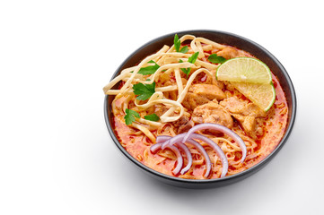 Khao Soi Gai or Thai Coconut Curry Noodle Soup in black bowl isolated on white background. Khao Soy is Thailand cuisine dish with noodles, chicken meat, red chillies paste and spices. Isolate