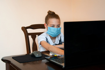 A schoolgirl in a medical mask looks into a laptop. Distance learning in quarantine. Home schooling. Internet e-learning