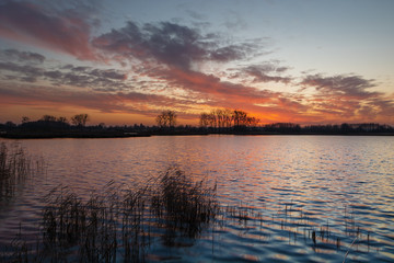 Fototapeta na wymiar Colorful clouds after sunset on the lake with reeds