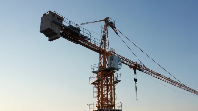 Yellow tower crane on a construction site, against clear blue sky, illuminated by late afternoon sun. Aerial footage.