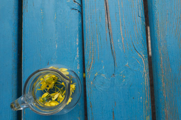 Many yellow flowers, small white flowers in a transparent glassy round vase on a blue wooden background. There is a place for text. Shabby chic style. Concept fot Valentine's Day, Mother's Day