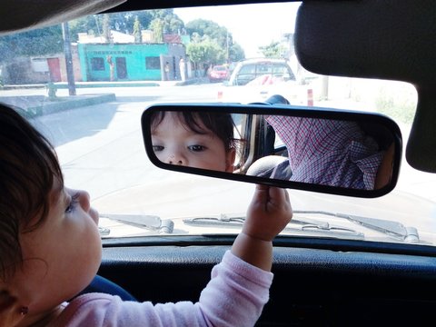 Reflection Of Baby Girl On Rear-view Mirror In Car