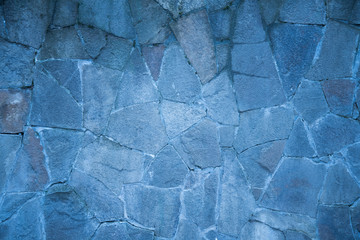 Close up hand crafted crooked old wall with many small and large stones like red sandstone and natural stones. cold blue shade. Background